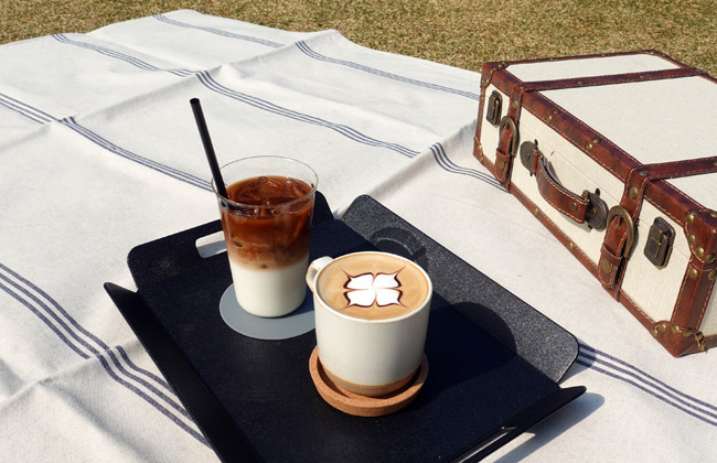 잔디 위 돗자리를 깔고 커피를 놓아둔 모습